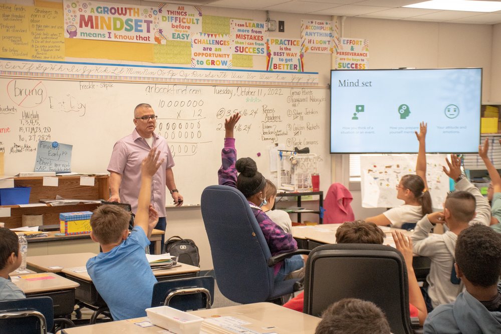 Students in class listening to teacher, raising their hand